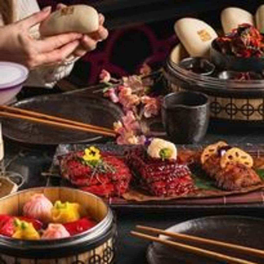 Tattu_Exquisite_Asian_Cuisine_Dining_Experience Alt text: "Assorted gourmet dishes at Tattu, featuring colorful dim sum in a steamer basket, beautifully presented sushi, and other Asian cuisine delicacies on a dark table setting with chopsticks and floral decorations."