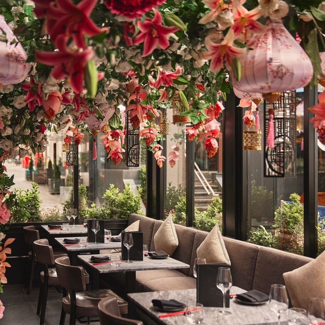 Tattu_FloralDecor_RestaurantAmbiance_ElegantDining Elegant dining area at Tattu with plush seating, set tables, and vibrant hanging floral decorations.