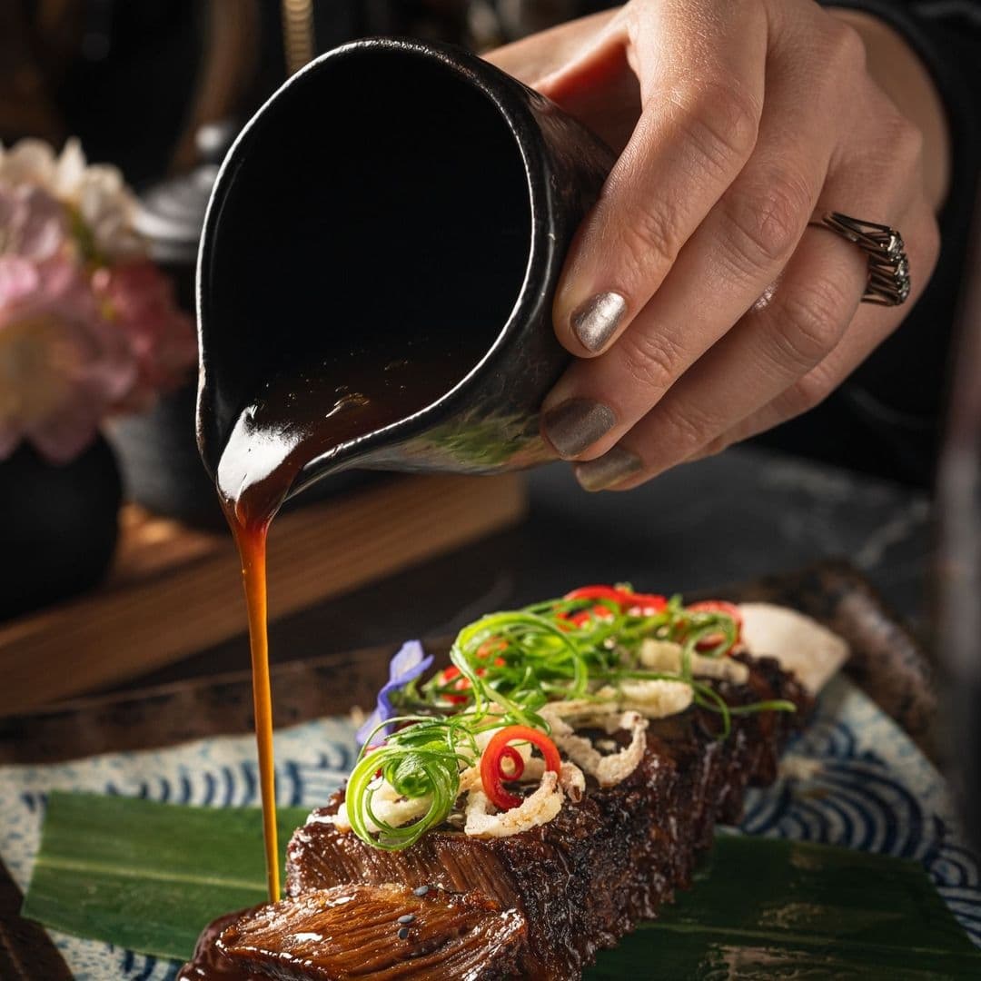 Tattu_Gourmet_Dish_Sauce_Pouring Close-up of a hand pouring sauce over a gourmet dish at Tattu restaurant.