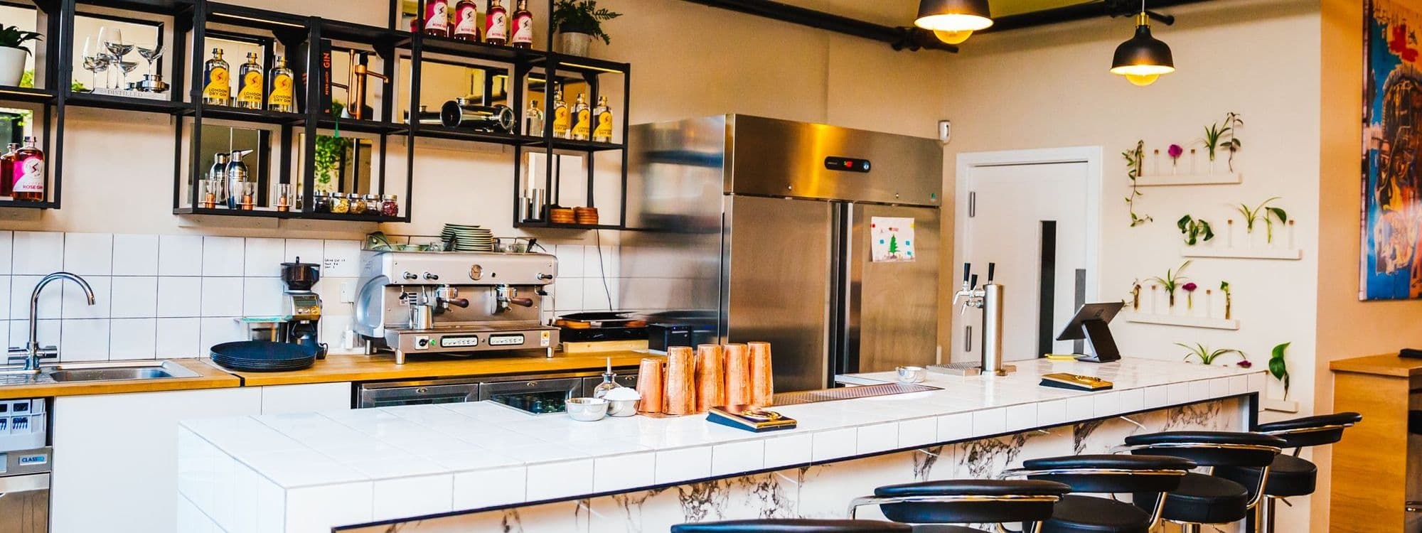 Interior view of Test Bar with a clean, modern bar counter, espresso machine, shelves with bottles, and bar stools.
