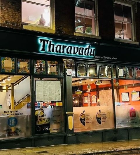 Tharavadu Kerala Cuisine Restaurant Nighttime Exterior Exterior view of Tharavadu restaurant at night, showcasing illuminated signage, award stickers, and cultural decorations in the windows.