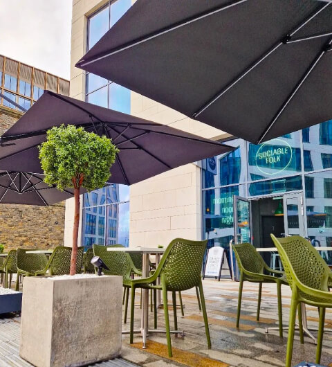 Sociable_Folk_Outdoor_Seating_Area Umbrellas Relaxed_Atmosphere Outdoor seating area at Sociable Folk with green chairs and large umbrellas, a potted tree, and a view of the cafe's entrance.