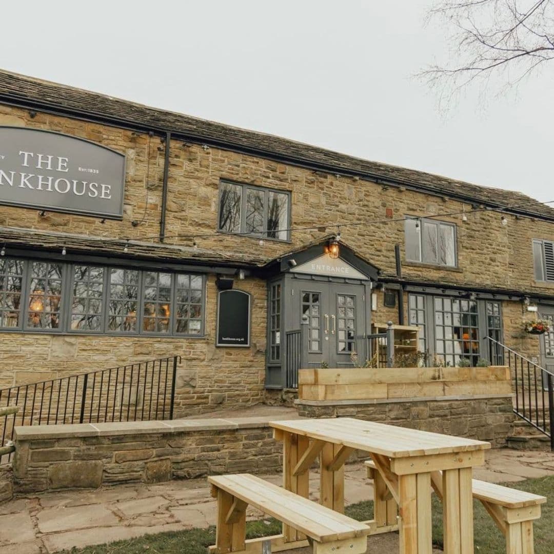 Bankhouse_Inn_Stone_Building_Exterior_Wooden_Benches Exterior view of the Bankhouse Inn with stone facade, wooden benches in the foreground, and entrance with lit signage.