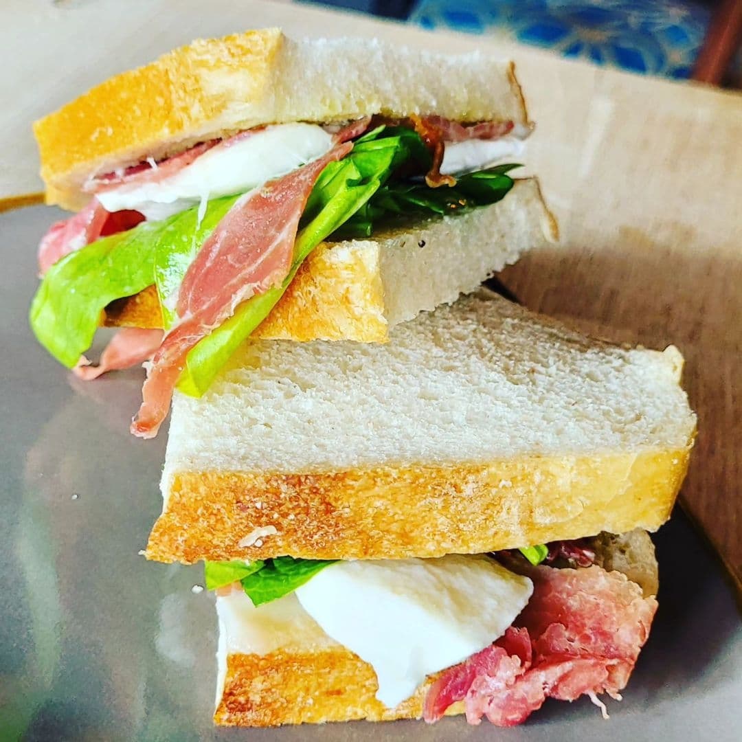 Pookys Deli Cafe Fresh Italian Sandwich Crispy Bread Freshly prepared sandwich with crusty bread, layered with prosciutto, mozzarella, and green lettuce served on a wooden plate at Pooky’s Deli & Cafe.