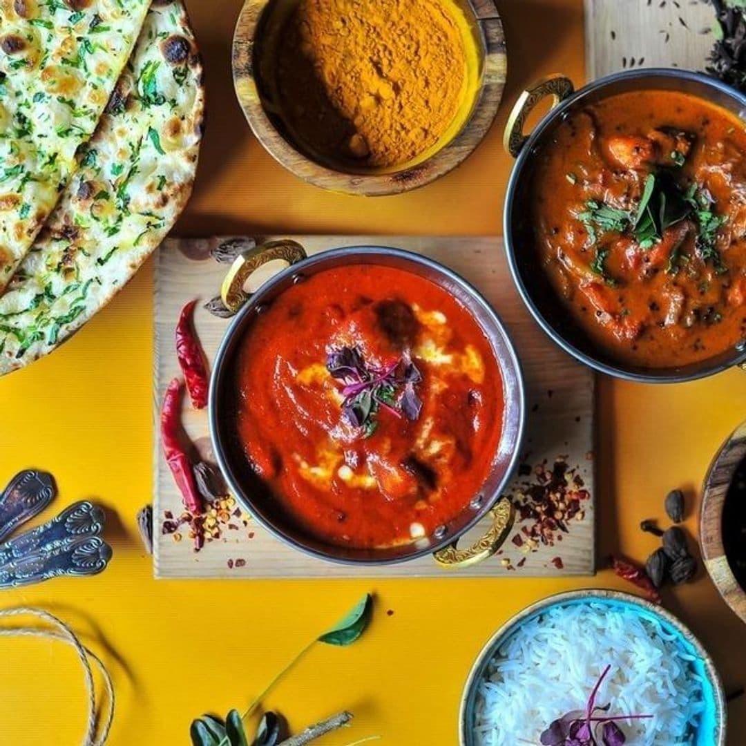 The Cats Pyjamas Chapel Allerton Indian Cuisine Colorful Dishes Top View Assorted Indian dishes on a vibrant yellow table at The Cat’s Pyjamas – Chapel Allerton, featuring butter chicken, naan bread, lentil curry, and basmati rice, garnished with herbs and spices.