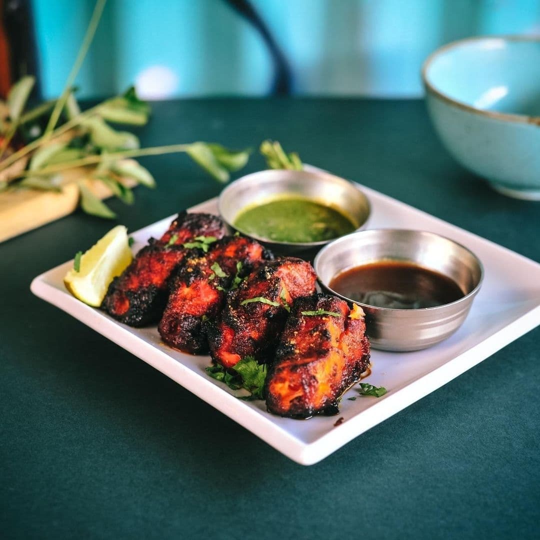 The Cats Pyjamas Chapel Allerton Indian Cuisine Tandoori Dish Sauces Succulent grilled chicken with charred edges served with lemon wedge, green chutney, and tamarind sauce on a white plate at The Cat’s Pyjamas – Chapel Allerton.