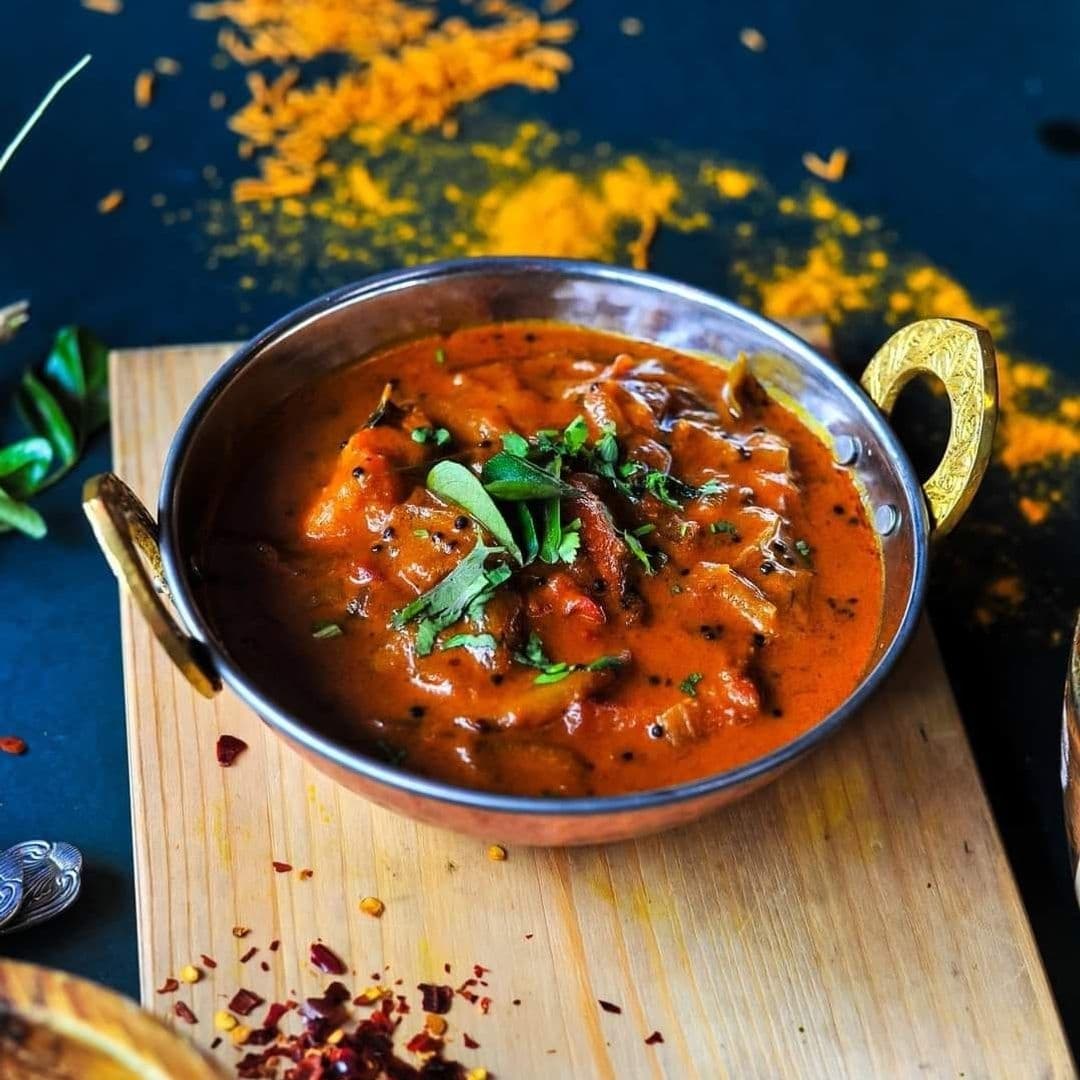 The Cats Pyjamas Farsley Authentic Indian Cuisine Curry Dish A bowl of rich, creamy curry garnished with fresh herbs served at The Cat’s Pyjamas – Farsley, with vibrant spices scattered in the background.