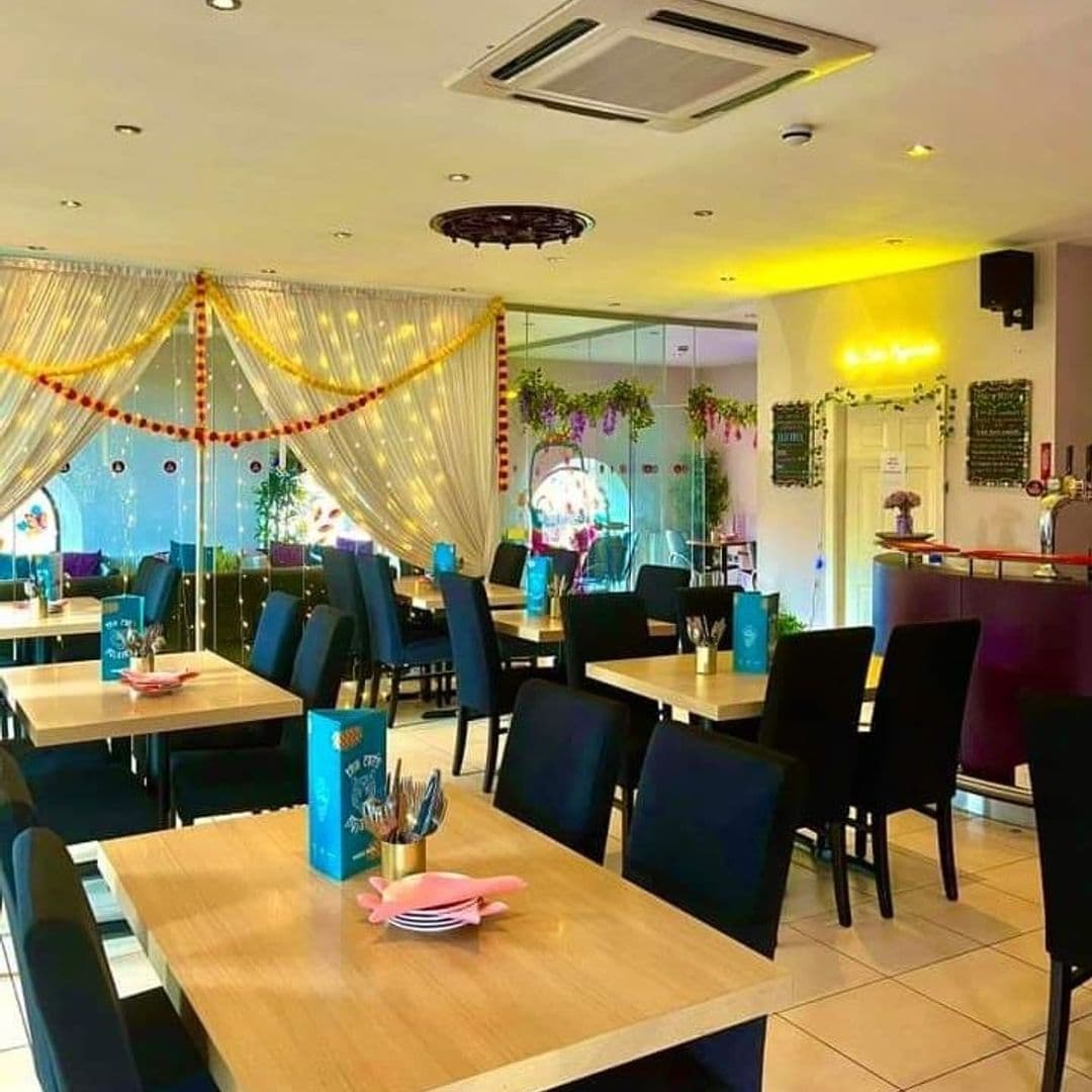 The Cats Pyjamas Farsley Colorful Interior Dining Area Decor Interior of The Cat’s Pyjamas – Farsley, showing a brightly lit dining area with wooden tables, black chairs, and festive decorations. A bar area is visible in the background.