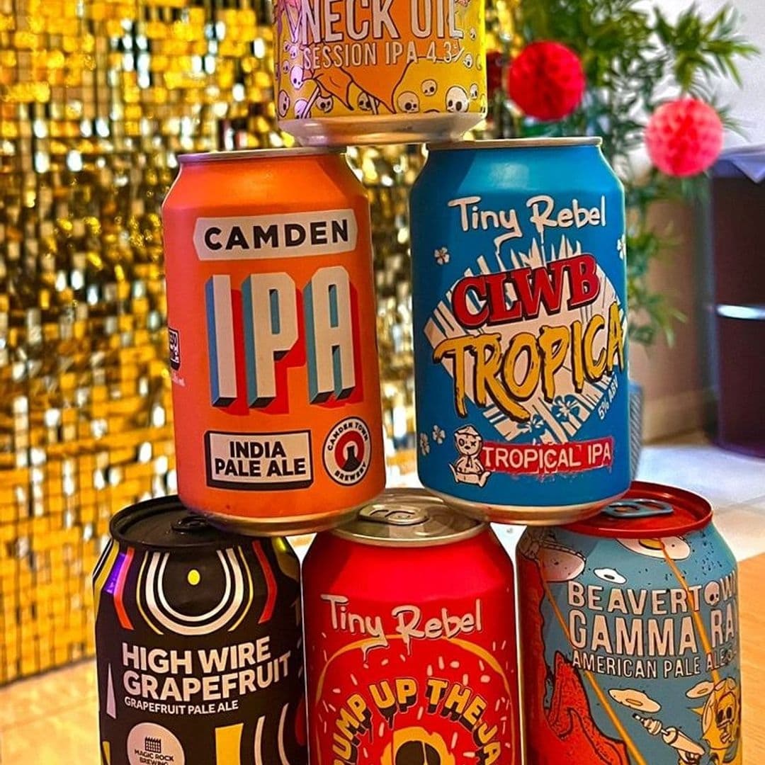 The Cats Pyjamas Farsley Craft Beer Selection Colorful Cans Assorted craft beer cans with vibrant designs displayed at The Cat’s Pyjamas – Farsley, featuring a golden sequin backdrop.