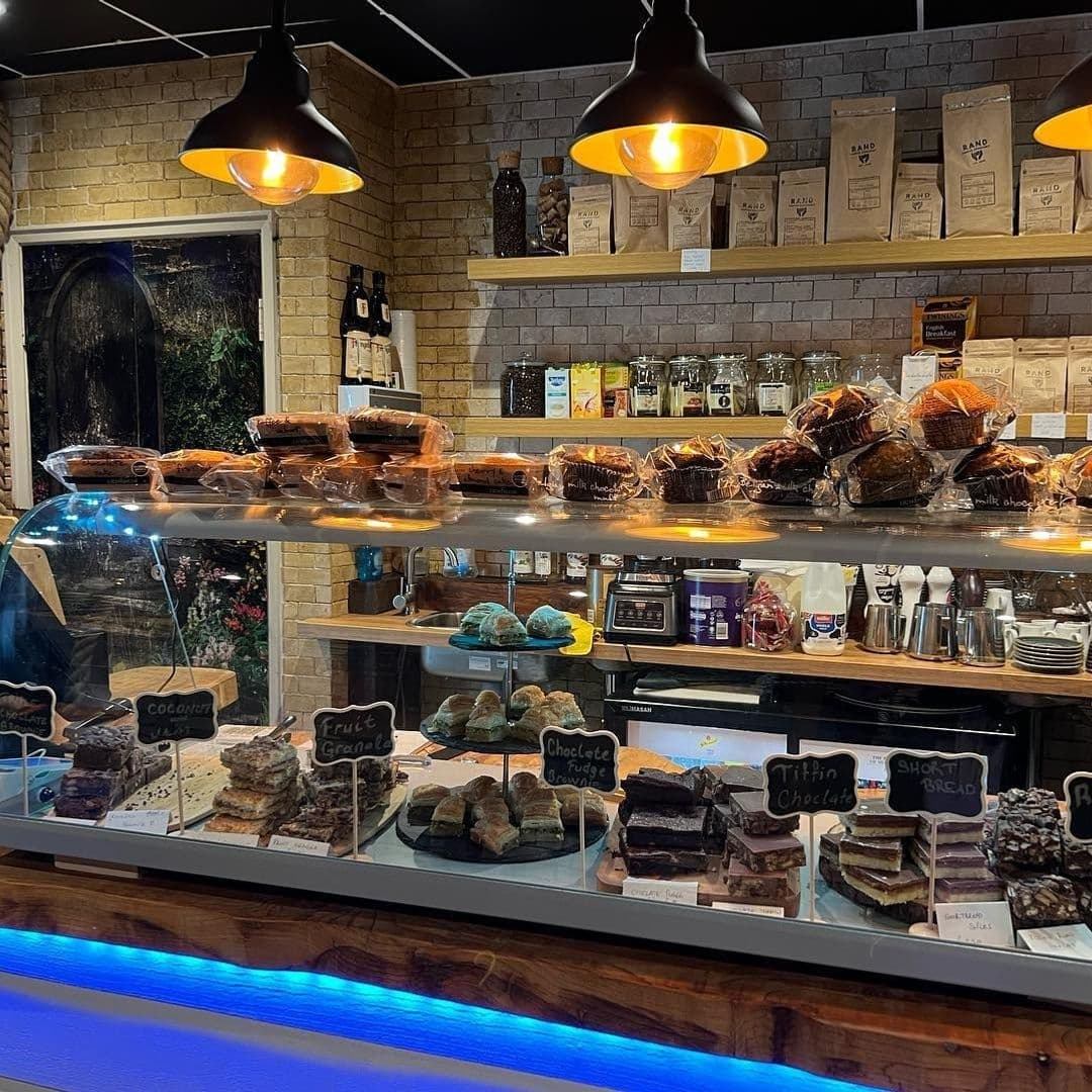 Unique Coffee Bistro Artisan Pastries Display Warm Ambiance Interior of Unique Coffee&Bistro showing a display case filled with assorted baked goods, including brownies and shortbread, under warm pendant lighting with shelves of coffee bags and bottles in the background.
