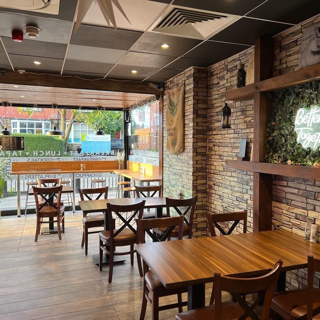 Unique Coffee Bistro Cozy Interior Brick Walls Wooden Furniture Interior of Unique Coffee&Bistro showing wooden tables and chairs, brick walls with decorative greenery, and a view of the street through the glass window.