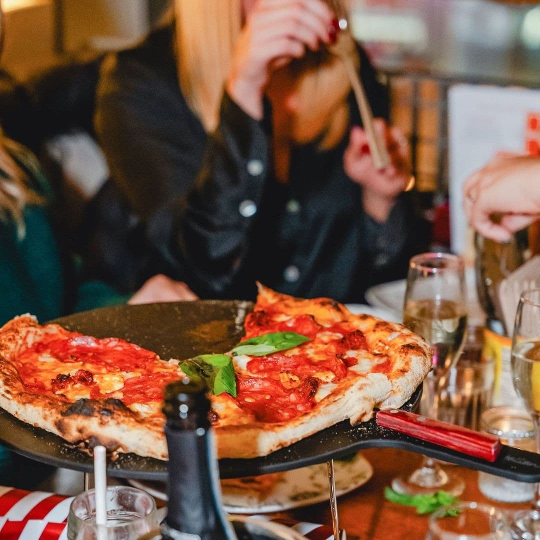LIVINItaly authentic italian pizza dining experience Alt text: "A freshly baked pizza with vibrant tomato sauce and melted cheese garnished with a basil leaf, presented on a table at LIVIN'Italy amidst diners enjoying their meal."