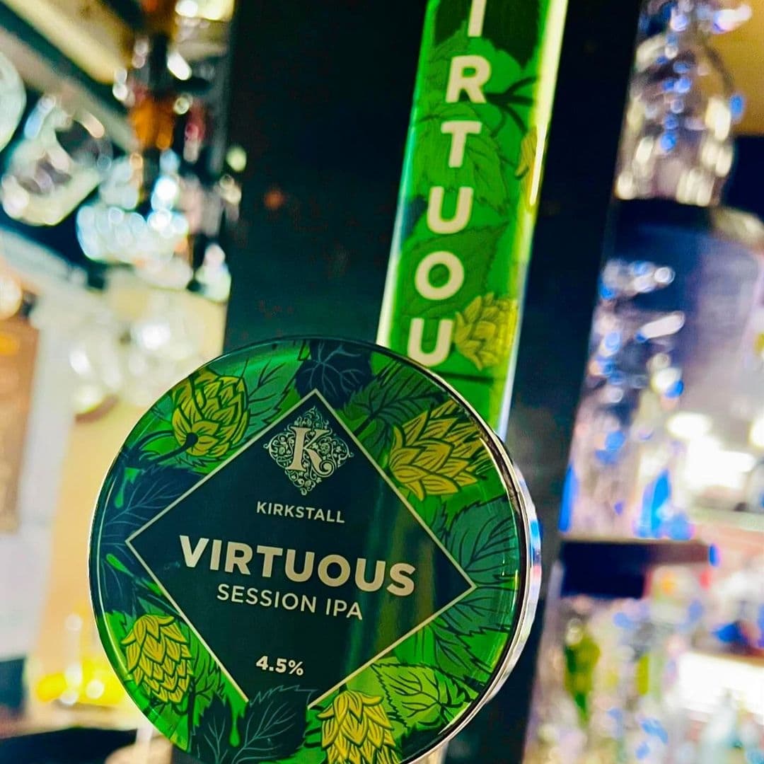 The Chequers Inn Kirkstall Virtuous IPA Pub Atmosphere Close-up of a Kirkstall Virtuous Session IPA beer tap at The Chequers Inn, with blurred background of bar interior.