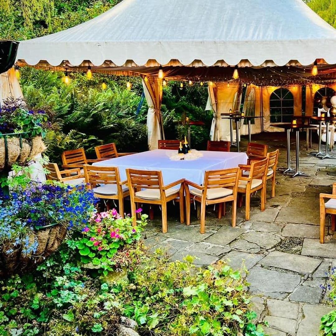 The Chequers Inn Outdoor Dining Area Twilight Lights Floral Decor Outdoor dining area at The Chequers Inn with wooden tables and chairs under a white canopy, surrounded by lush greenery and colorful flowers.