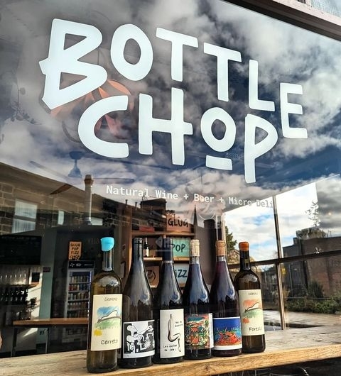 BottleChop WineShop WindowDisplay SunnyDay Window display at Bottle Chop featuring an array of natural wine and beer bottles with a clear view of the shop's interior, under the large white text logo on the window.