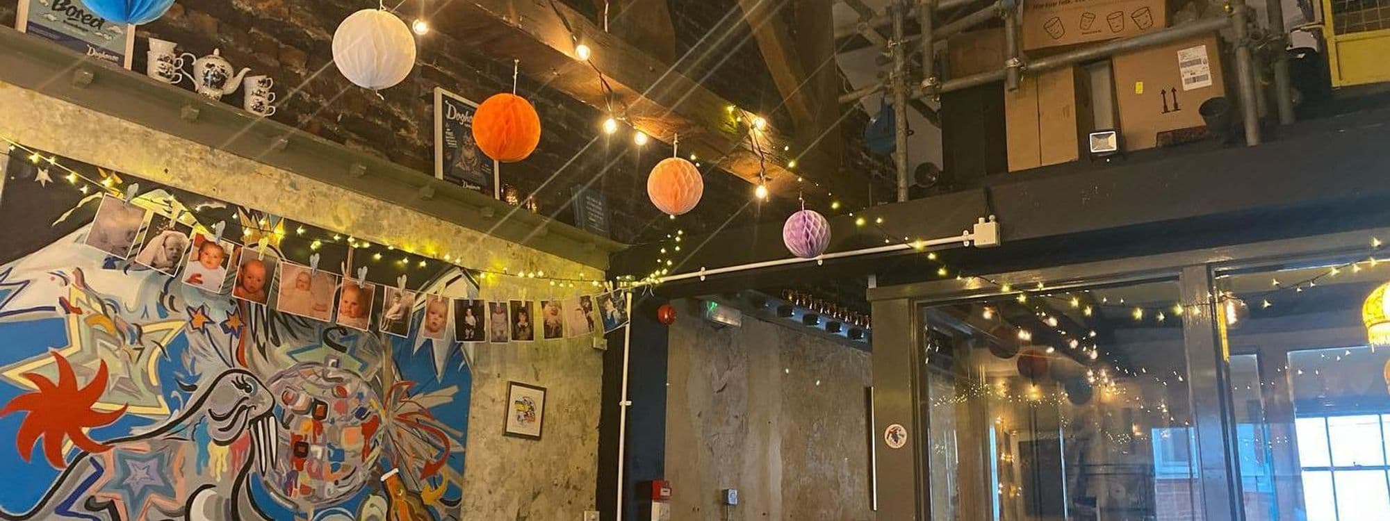 Interior of Doghouse Bar & Bagel Shop featuring eclectic decor with string lights, colorful paper lanterns, and a vibrant mural with whimsical designs.