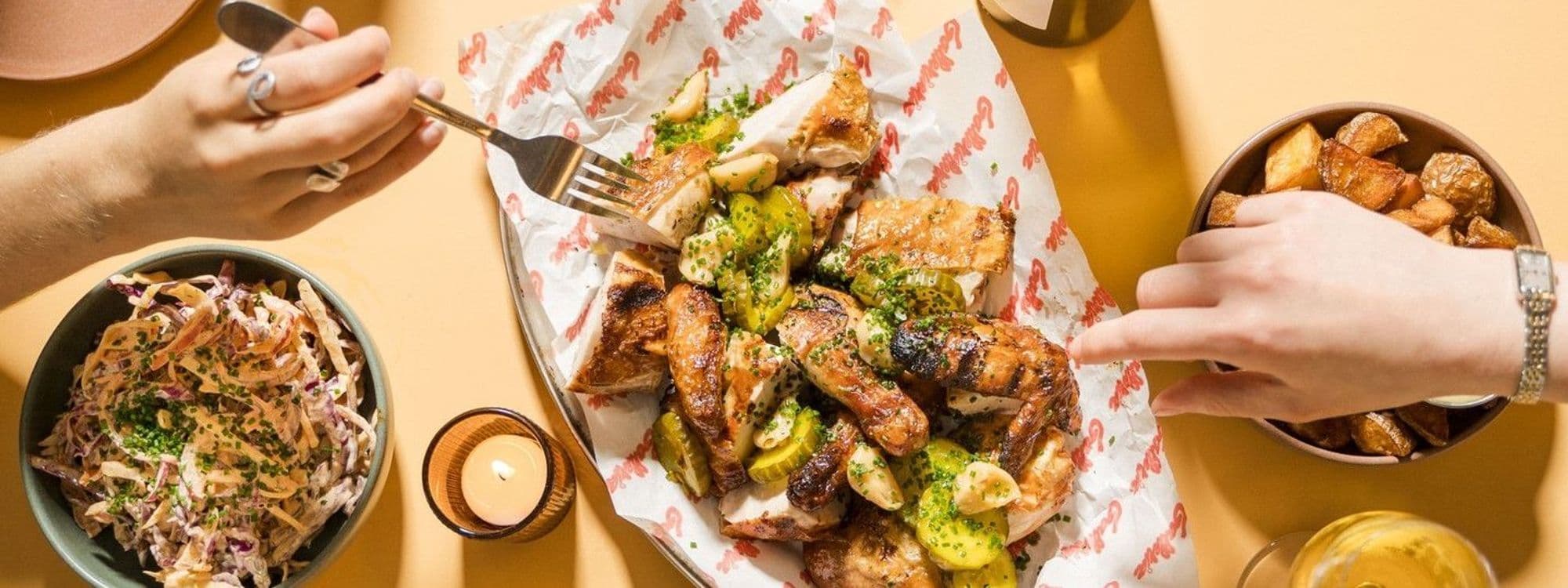 Alt text: "Dining experience at Galleria featuring a table with a delicious spread of roasted chicken, sliced pickles, and roasted potatoes, complemented by a bowl of coleslaw and a lit candle, capturing a cozy and appetizing meal setting."
