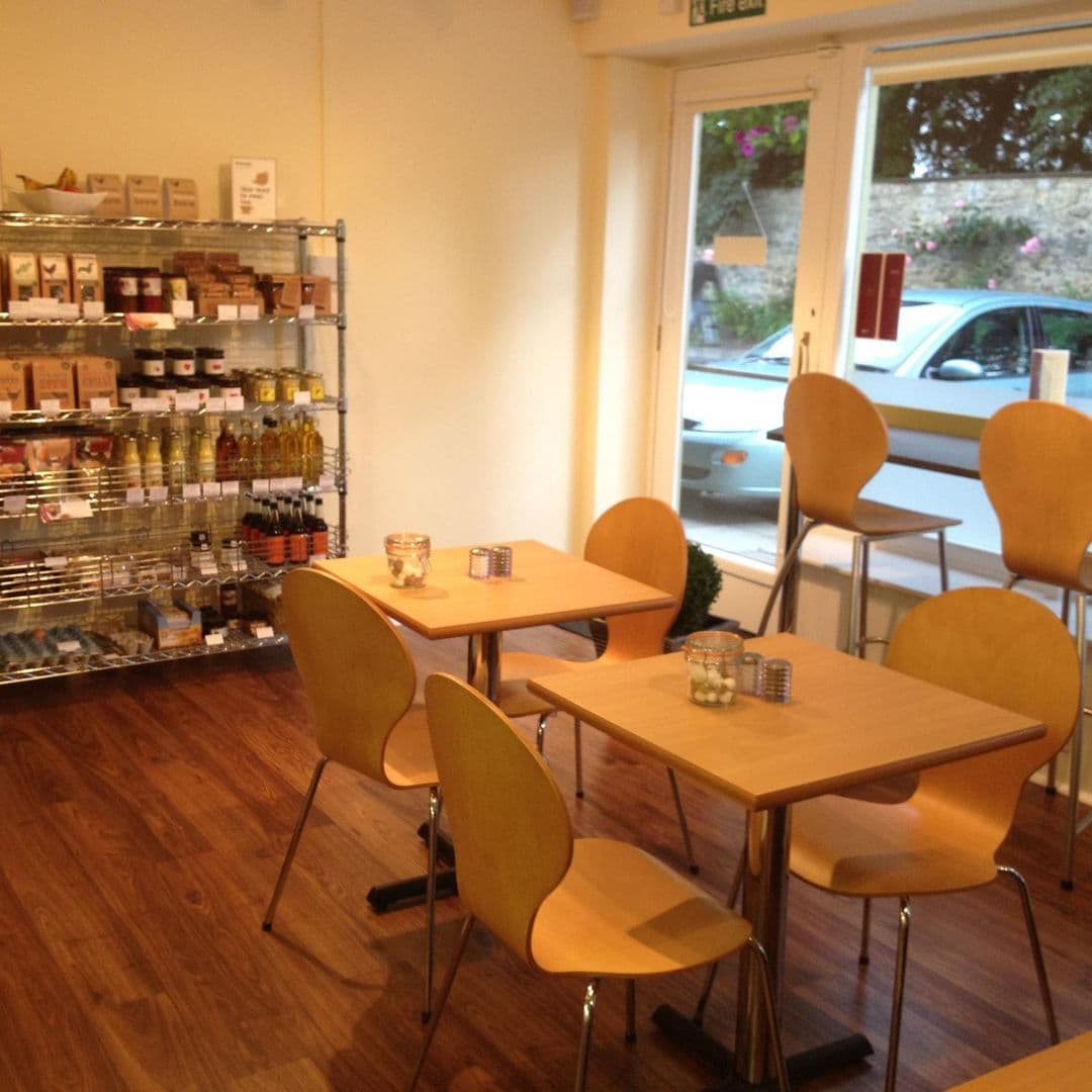 Maypole Coffee Shop Deli Cozy Interior Tables Products Interior of Maypole Coffee Shop & Deli with wooden tables, yellow chairs, and shelves stocked with gourmet products.