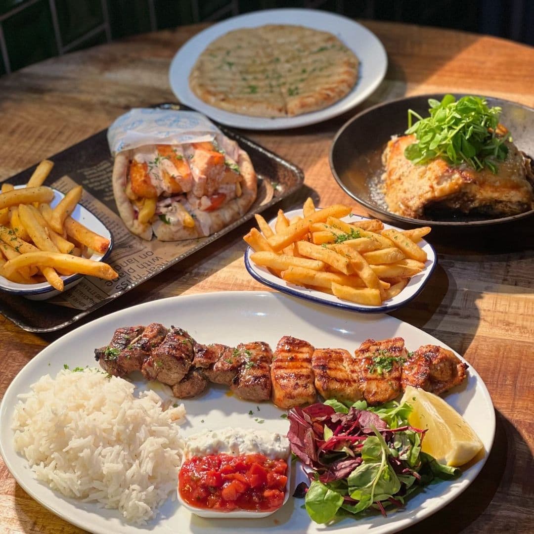 Santorini Bar and Grill Delicious Mediterranean Meals Assorted Greek dishes at Santorini Bar and Grill, featuring skewered grilled meat with rice, tzatziki, and salad, a wrapped gyro with fries, a pizza, and a chicken dish topped with arugula.