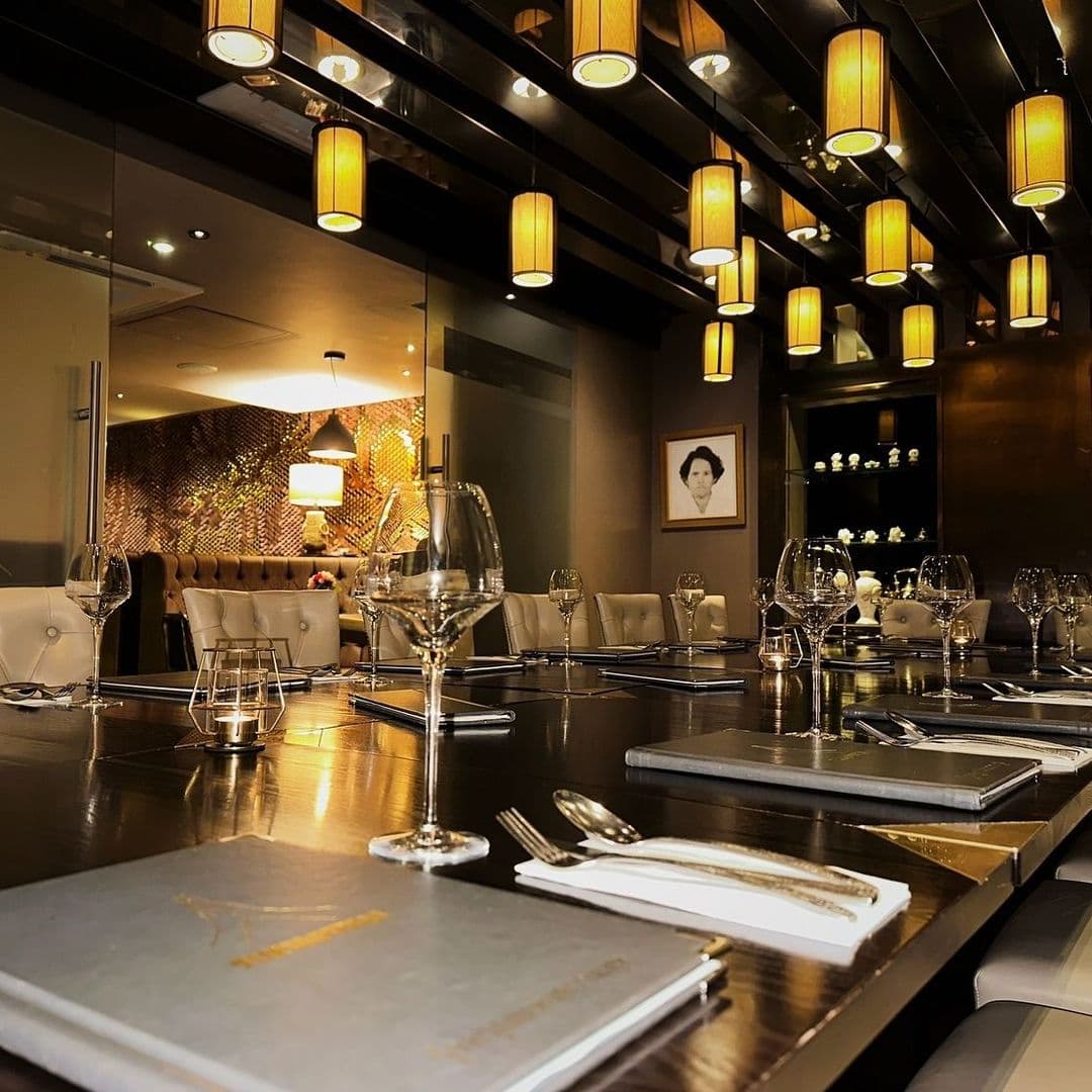 Sukhothai Restaurant City Centre Elegant Dining Atmosphere Elegant dining setup at Sukhothai Restaurant – City Centre, featuring neatly arranged tables with wine glasses, cutlery, and menus under warm pendant lighting.