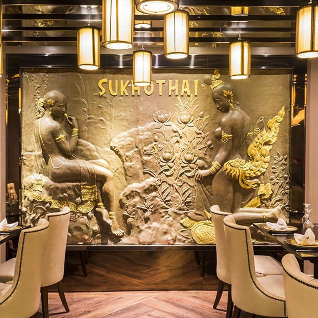 Sukhothai Restaurant City Centre Elegant Interior Thai Artwork Dining Ambiance Elegant dining area at Sukhothai Restaurant – City Centre, featuring a large golden bas-relief wall art with traditional Thai figures, surrounded by chic hanging lanterns and plush seating.