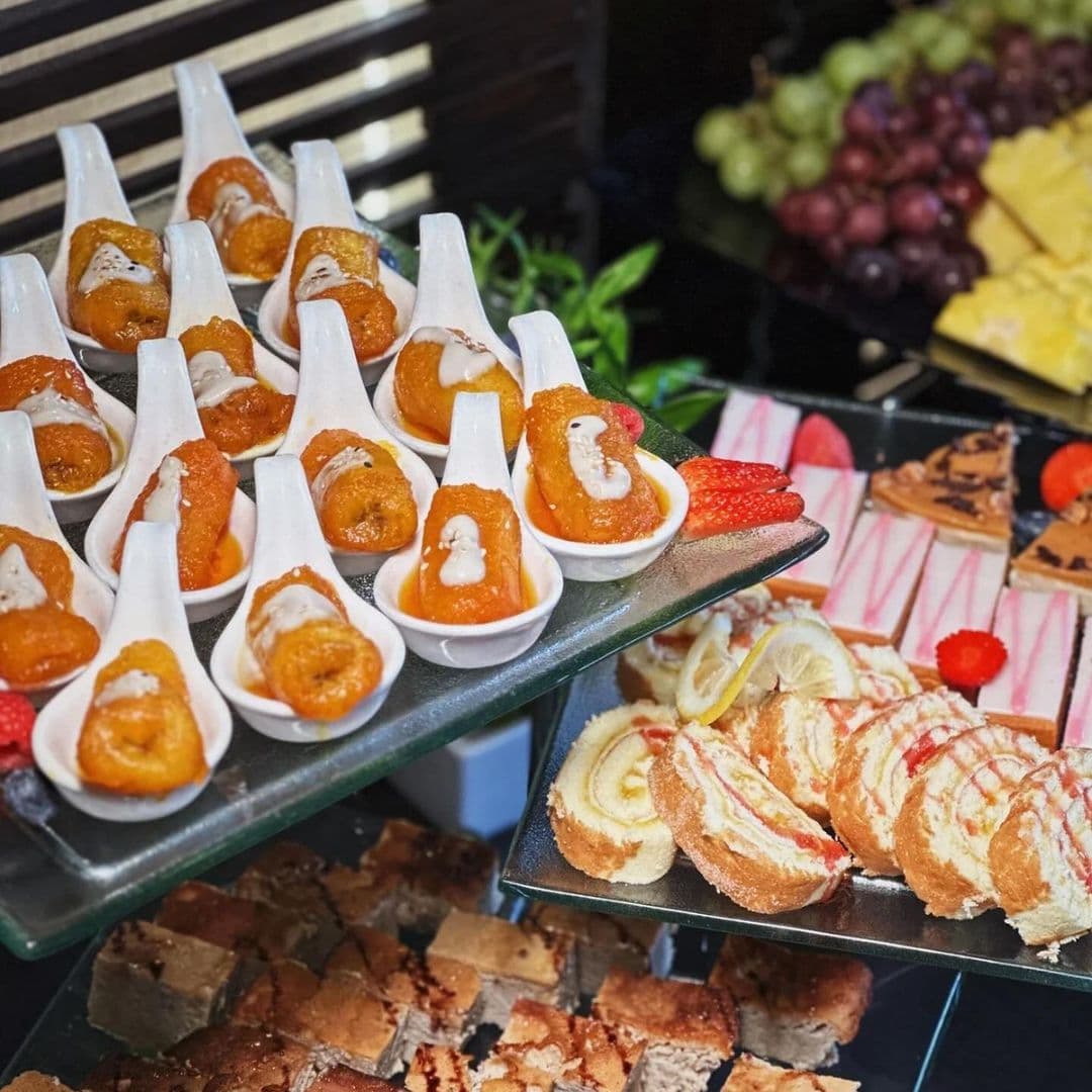 Sukhothai Restaurant City Centre Gourmet Dessert Buffet Selection Assorted desserts on display at Sukhothai Restaurant – City Centre, featuring spoonfuls of golden syrupy sweets, sliced cake rolls with cream and strawberries, and a selection of fresh fruit and chocolate treats.