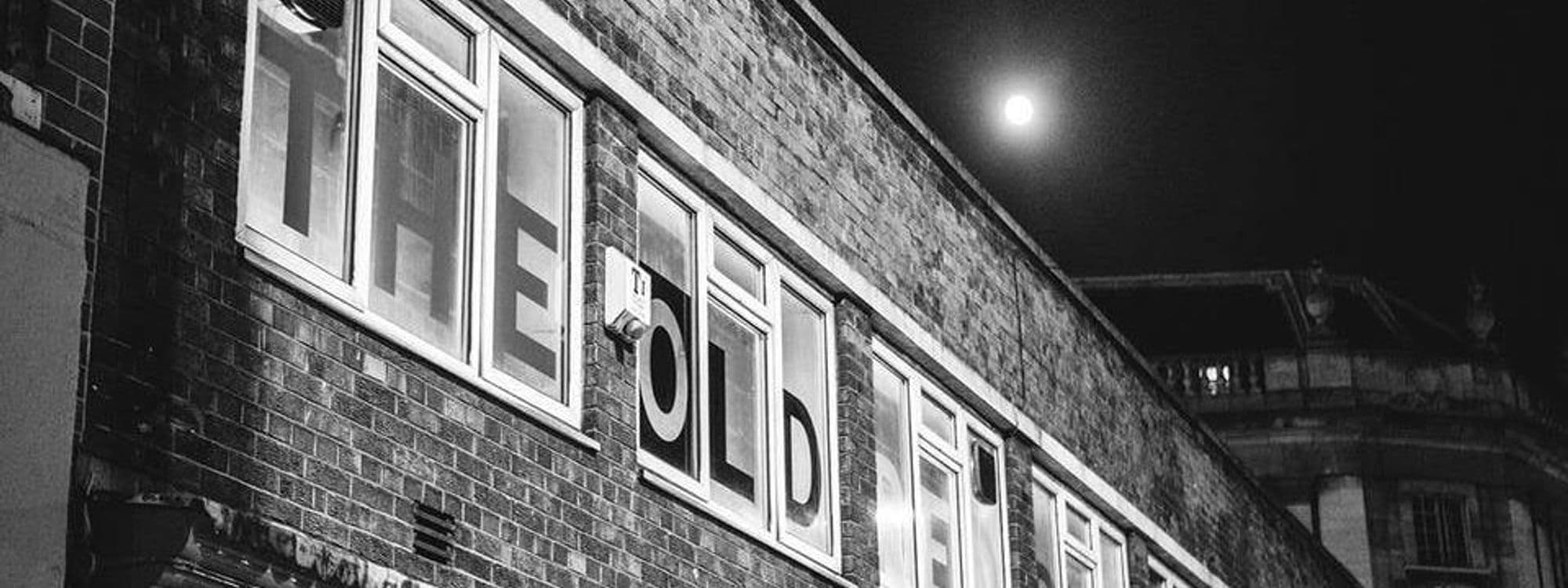 Exterior view of The Old Red Bus Station at night, featuring the illuminated signage on the brick facade with a full moon in the background.