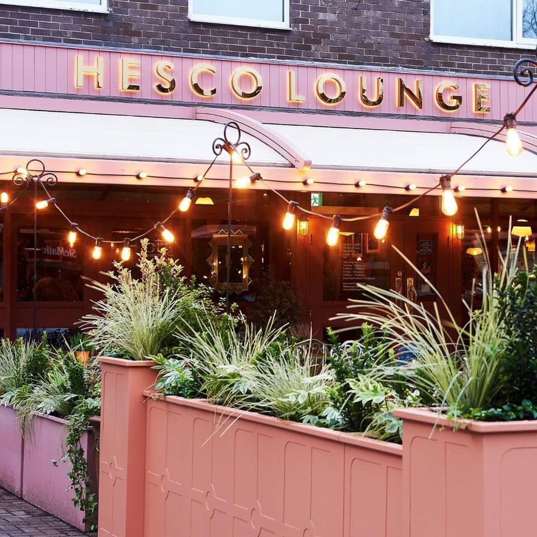 Hesco Lounge Evening Ambiance String Lights Exterior Exterior view of Hesco Lounge with illuminated signage, string lights, and green plants on the patio.
