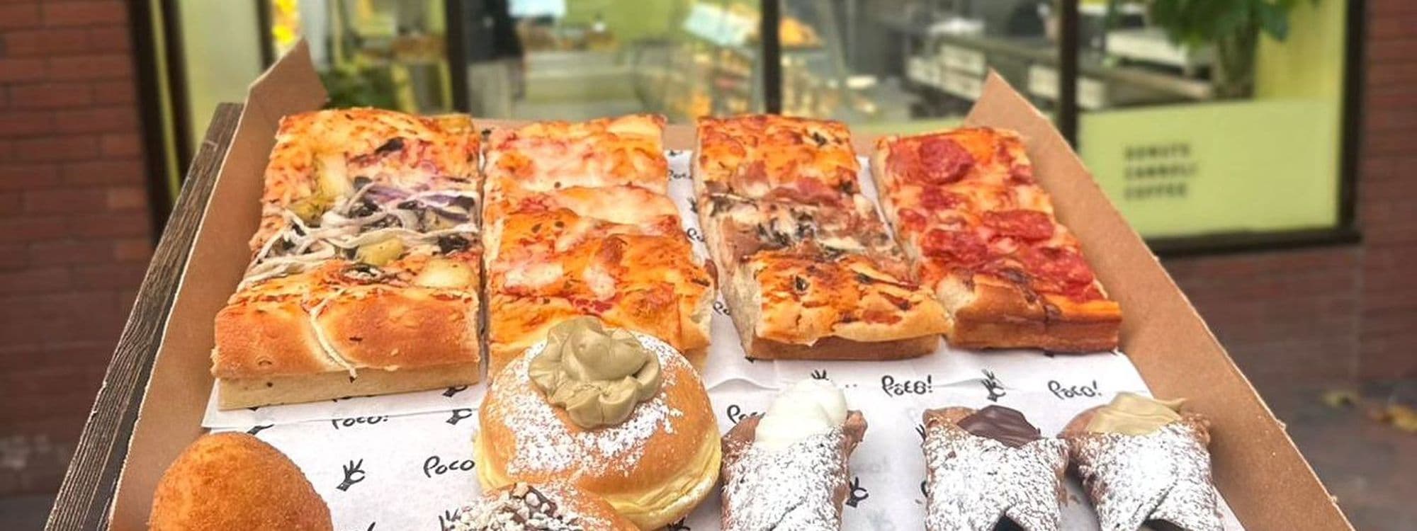 Assorted Sicilian street food from POCO Sicilian Street Food – The Calls, featuring slices of thick-crust pizza with various toppings and traditional Sicilian pastries dusted with powdered sugar, presented in a cardboard tray.