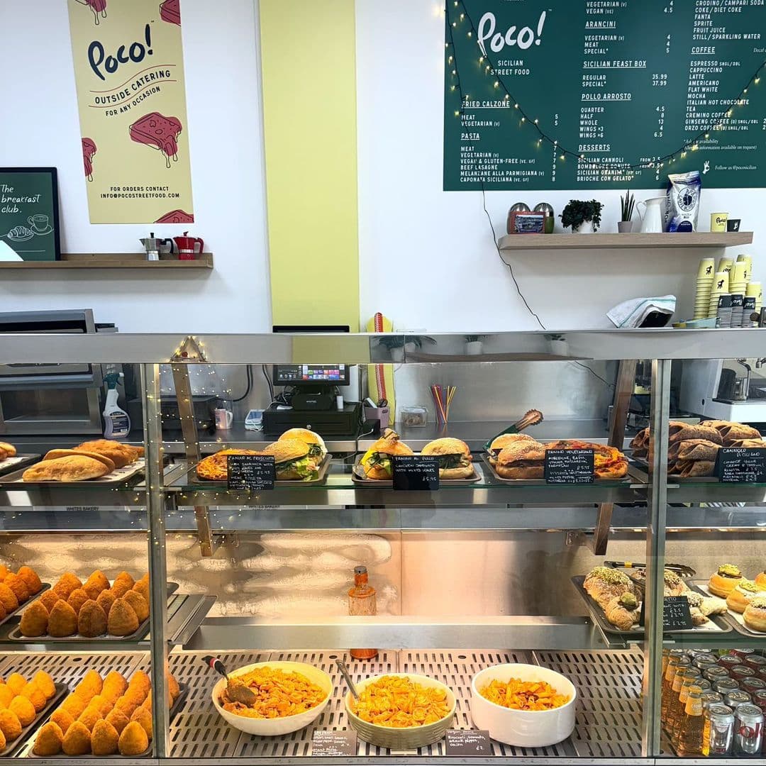 POCO Sicilian Street Food The Calls Delicious Display Counter Interior of POCO Sicilian Street Food – The Calls, showing a food display counter with various Sicilian pastries, sandwiches, and pasta dishes, and a menu board in the background.
