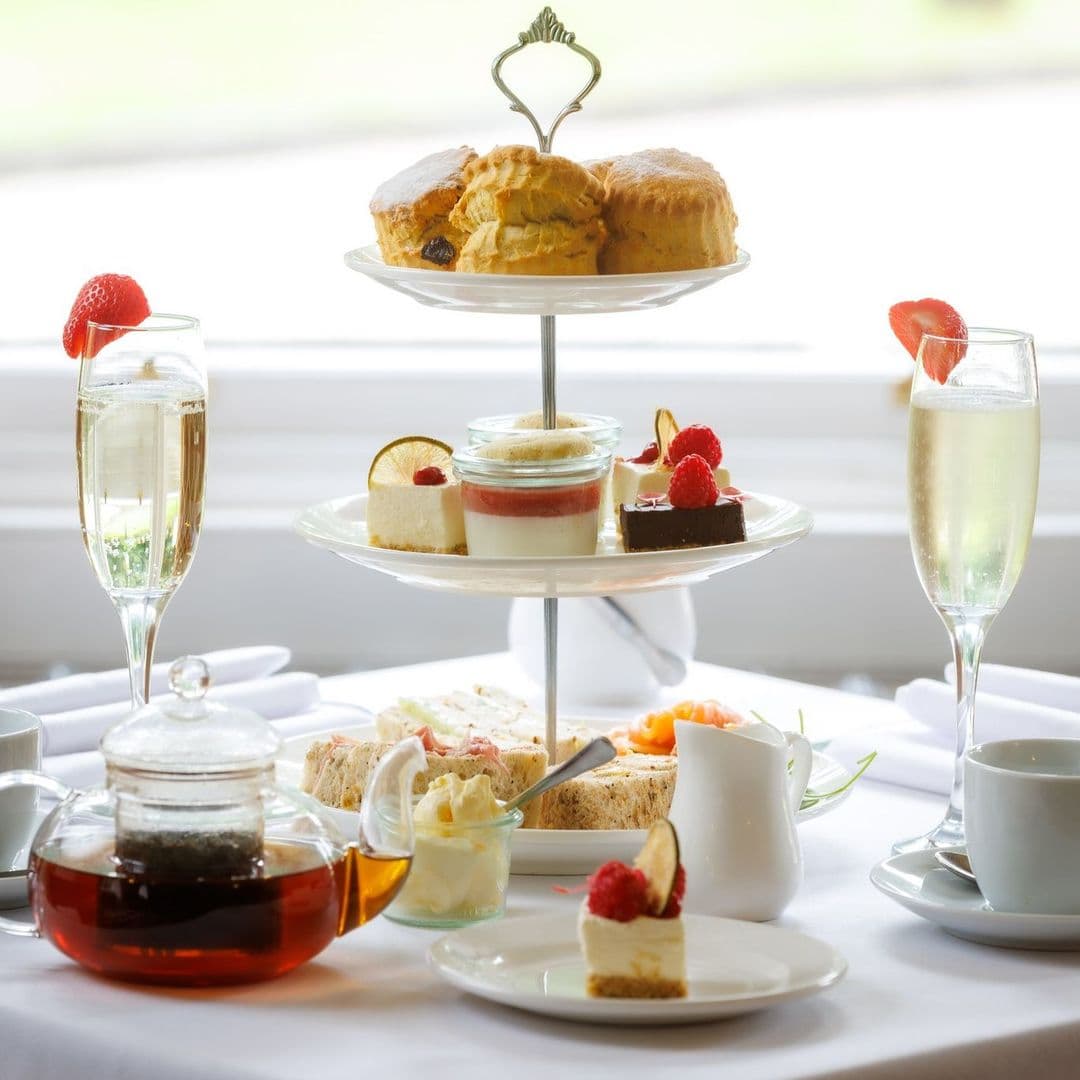 Convive Restaurant afternoon tea delicious desserts elegant setting A beautifully arranged afternoon tea set at Convive Restaurant, featuring a tiered stand with scones, assorted pastries, and desserts. There are two glasses of sparkling wine and a teapot filled with tea, alongside a small dish of cream and a plate of sandwiches. The setting is elegant and inviting, perfect for a relaxing dining experience.