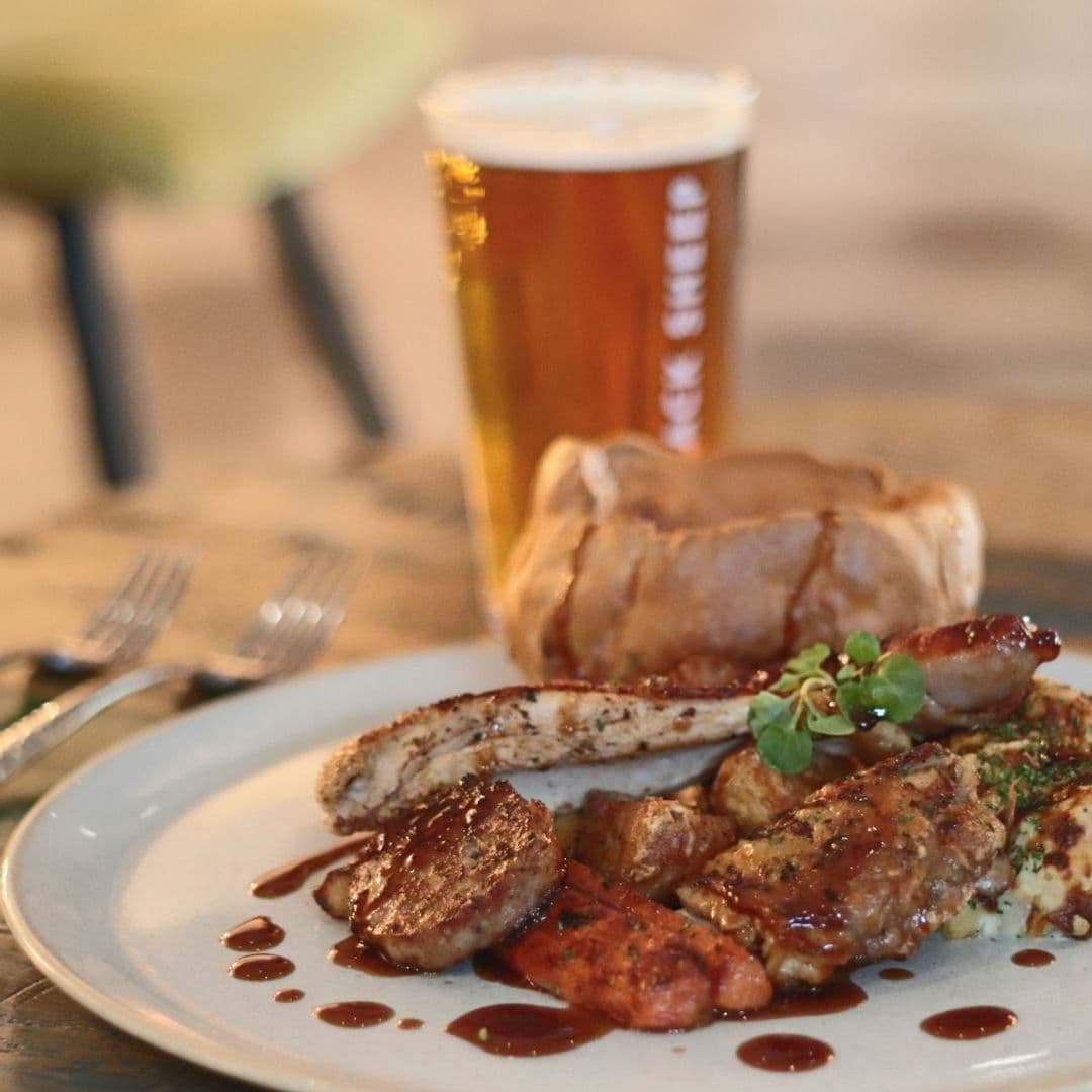 Convive Restaurant delicious food gourmet dining beer platter A delicious plate of mixed grilled meats, including sausages and chicken, served with roasted vegetables and a rich sauce, alongside a pint of beer at Convive Restaurant.