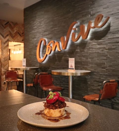 Convive Restaurant gourmet dish interior dining experience Delicious dish served at Convive Restaurant, featuring tender meat topped with fresh herbs and garnished with red peppers, set against a stylish backdrop with the restaurant's name in warm lighting.