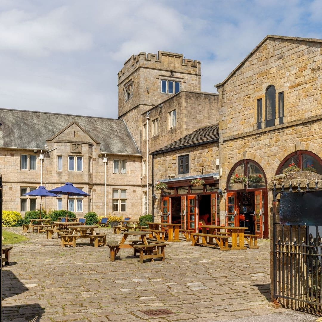 Convive Restaurant outdoor seating historic building sunny day Alt text: Outdoor seating area at Convive Restaurant, featuring wooden tables and umbrellas, surrounded by stone buildings and a historic tower under a partly cloudy sky.