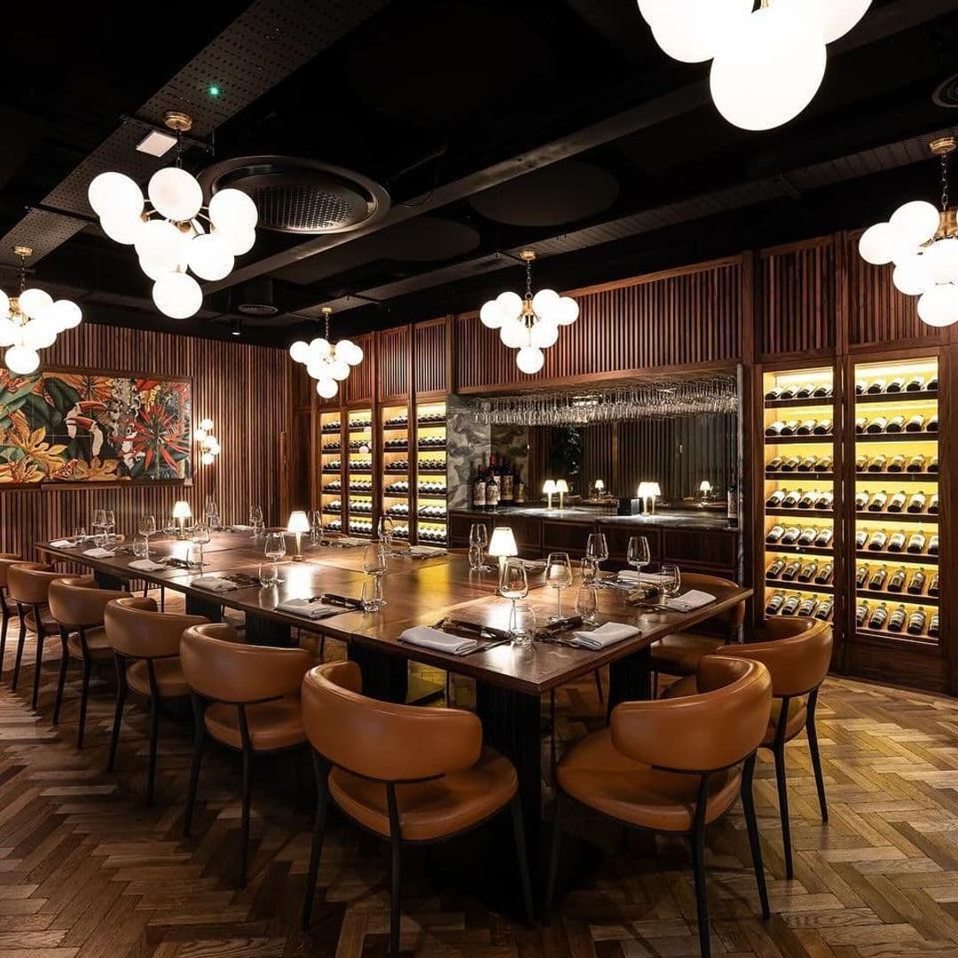 Fazenda Bar Grill elegant dining interior wine selection modern lighting **Alt Text:** Interior of Fazenda Bar & Grill featuring a large wooden dining table surrounded by stylish chairs. The room is illuminated by modern pendant lights and has a wine display on the wall. A vibrant painting adds a touch of color to the warm, inviting atmosphere.