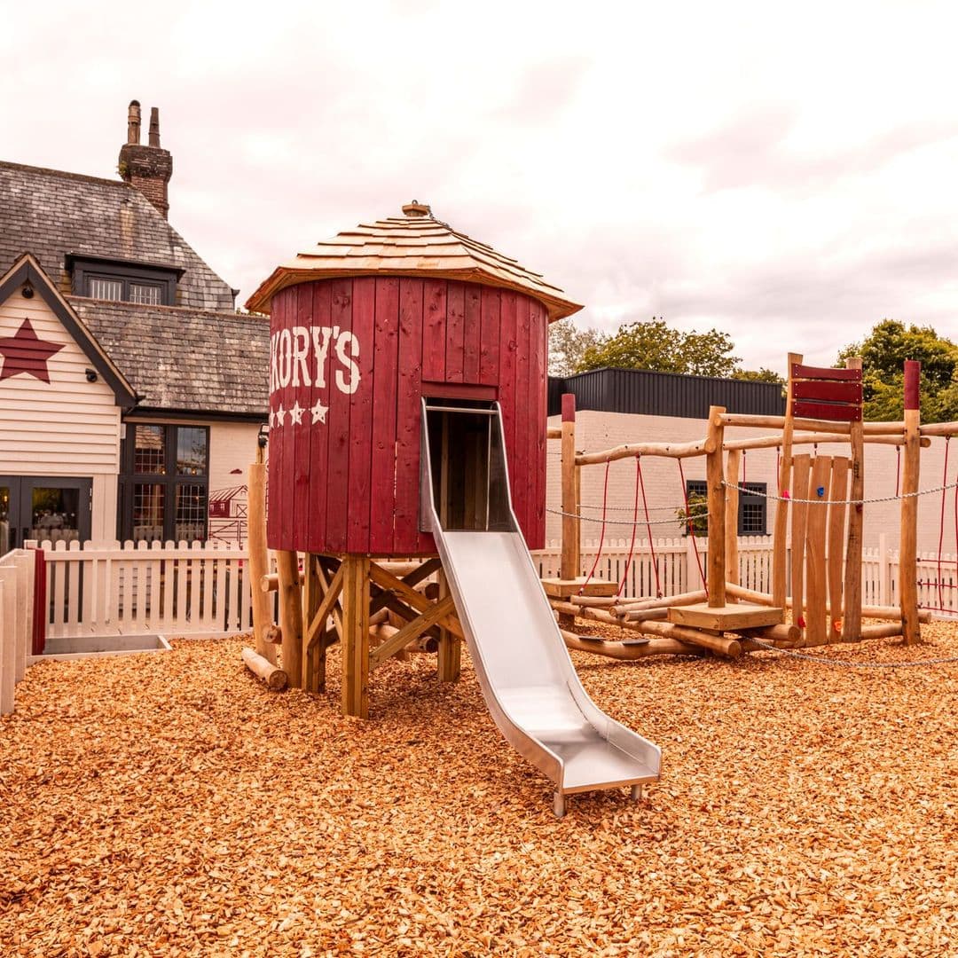 Fazenda Bar Grill playground slide red structure kids fun Playground area at Fazenda Bar & Grill featuring a red playhouse with a slide and wooden climbing structures surrounded by wood chips.