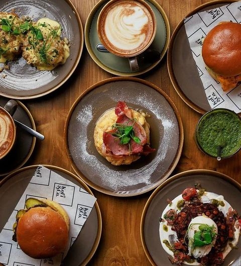 Kofi Co Roundhay gourmet food coffee brunch dining experience Delicious spread of food and drinks at Kofi&Co – Roundhay, featuring coffee, savory dishes, and fresh ingredients. The table is arranged with plates of burgers, eggs, and a vibrant green sauce, showcasing a variety of flavors.