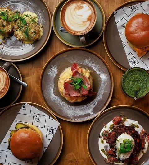 Kofi Co Roundhay gourmet food coffee brunch dining experience Delicious spread of food and drinks at Kofi&Co – Roundhay, featuring coffee, savory dishes, and fresh ingredients. The table is arranged with plates of burgers, eggs, and a vibrant green sauce, showcasing a variety of flavors.