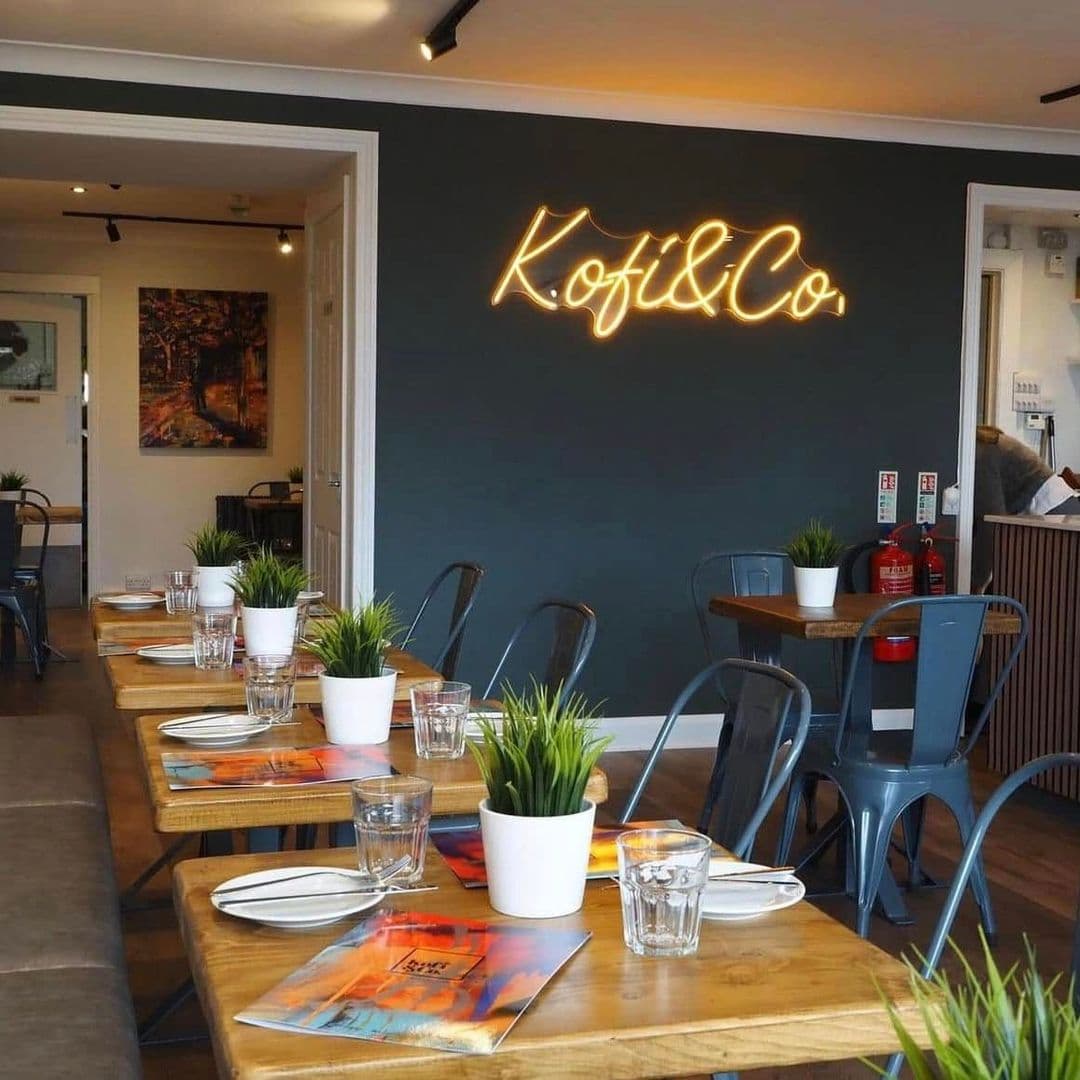 Kofi Co Wetherby cozy restaurant interior modern dining ambiance Alt text: Interior of Kofi&Co – Wetherby featuring wooden tables set with plates and glasses, small potted plants, and a stylish neon sign on the wall. The space is bright and inviting, perfect for dining.