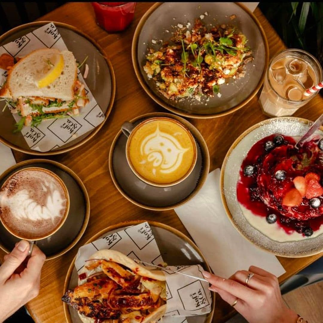 Kofi Co Wetherby delicious food coffee dessert dining Delicious food and drinks at Kofi&Co – Wetherby. The image features a variety of dishes including a sandwich, a colorful salad, and a dessert topped with berries. There are also two cups of coffee with latte art, showcasing a cozy dining experience.