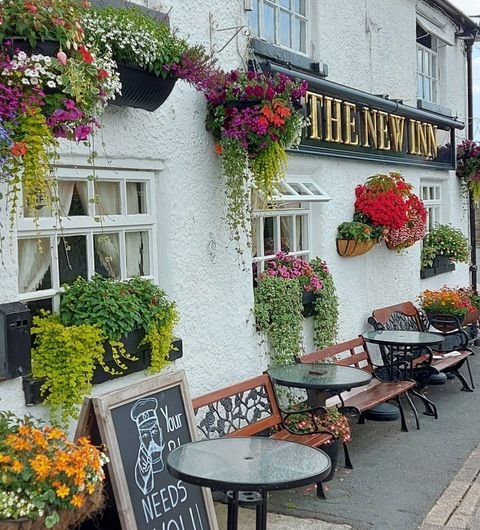 New Inn Barwick in Elmet charming pub flower baskets outdoor seating Alt text: Exterior view of The New Inn in Barwick in Elmet, featuring vibrant flower displays above the windows and on the walls. There are outdoor tables and chairs set up for guests, creating a welcoming atmosphere. A chalkboard sign is visible, adding to the charm of the pub.