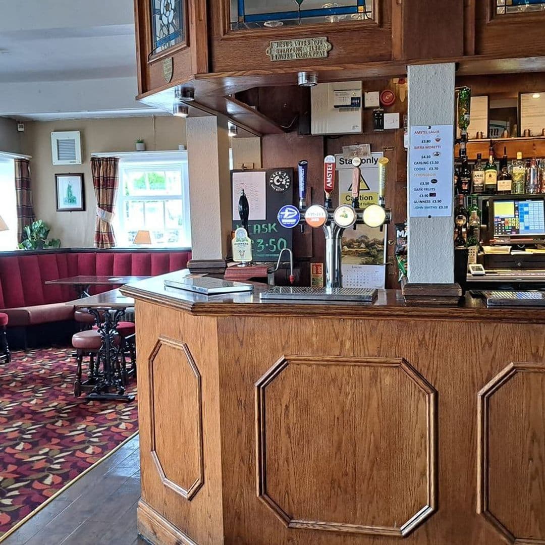 New Inn Yeadon bar interior cozy atmosphere local drinks Alt text: Interior view of the bar at New Inn – Yeadon, featuring wooden furnishings, a variety of beer taps, and a cozy seating area with red upholstery.