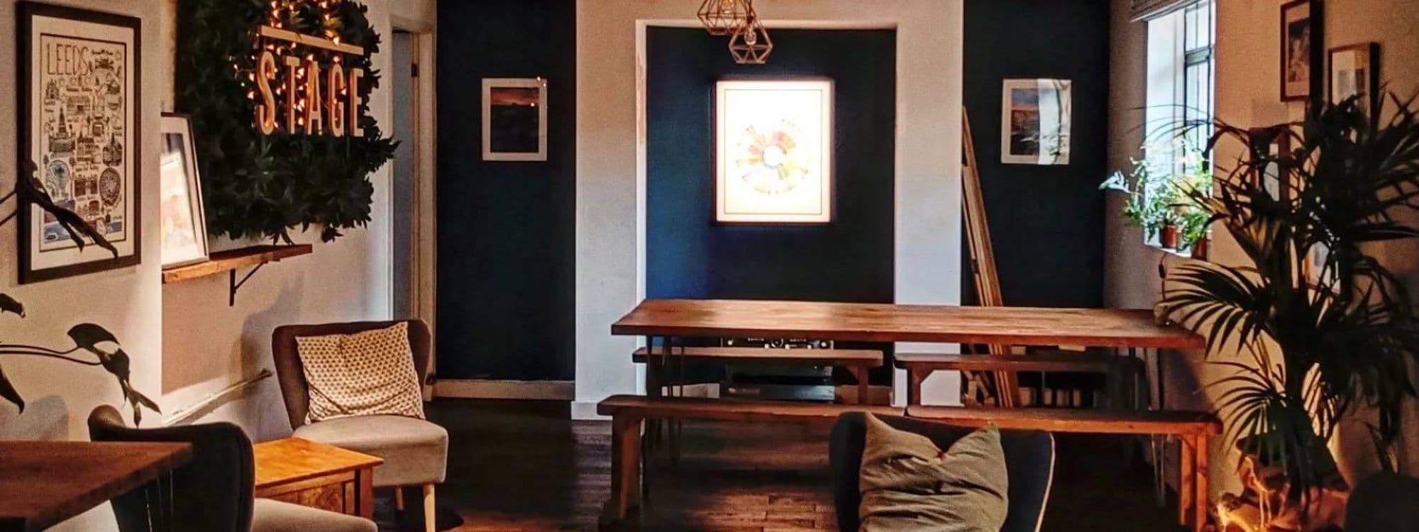Cozy interior of Stage Espresso & Brewbar featuring wooden tables, comfortable seating, and decorative plants. The walls are adorned with framed artwork, creating a warm and inviting atmosphere for visitors.