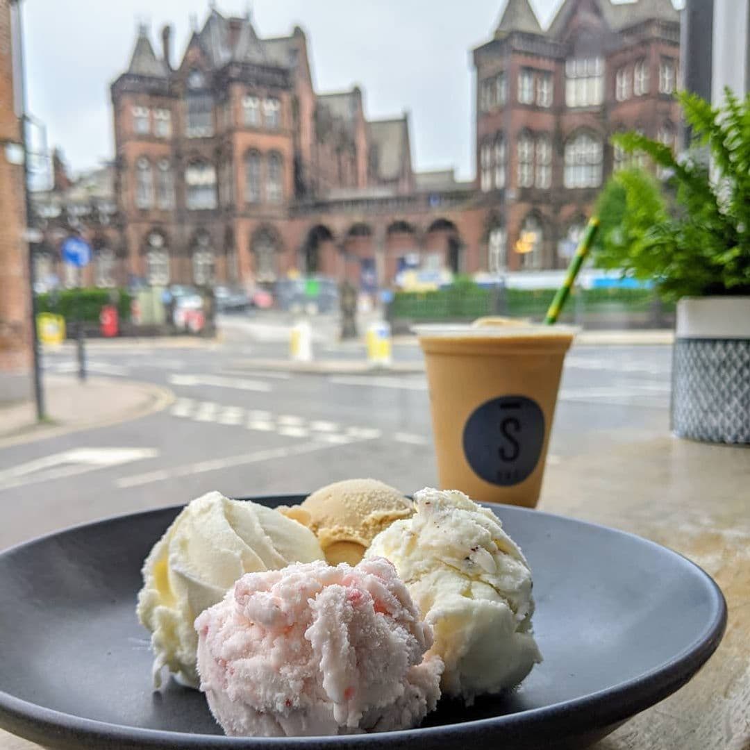 Stage Espresso Brewbar ice cream coffee treats cafe view A plate of assorted ice cream scoops in front of a window at Stage Espresso & Brewbar, with a coffee drink beside it. The background features a historic building and a street scene.