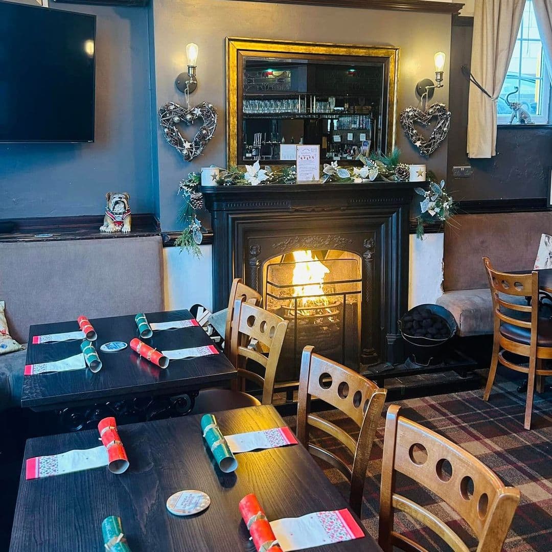 The Hare and Hounds Rothwell cozy fireplace dining restaurant interior warmth Cozy interior of The Hare and Hounds – Rothwell, featuring a warm fireplace, wooden tables set for dining, and festive decorations. The atmosphere is inviting, perfect for a relaxing meal.