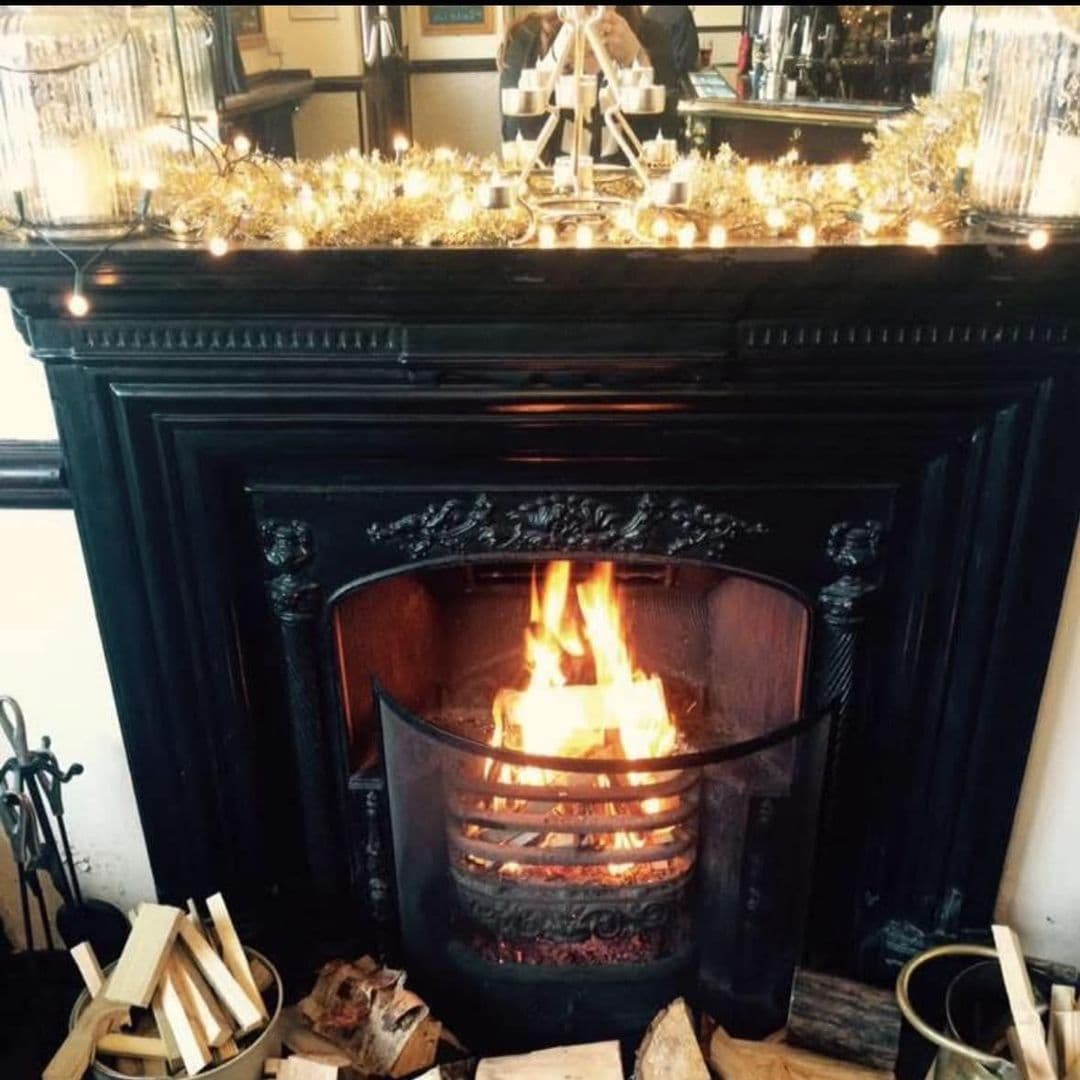 The Hare and Hounds Rothwell cozy fireplace warmth relaxation holiday decor Cozy fireplace with a warm fire, surrounded by logs and decorative lights. The setting exudes a welcoming atmosphere, perfect for relaxation. The Hare and Hounds – Rothwell.