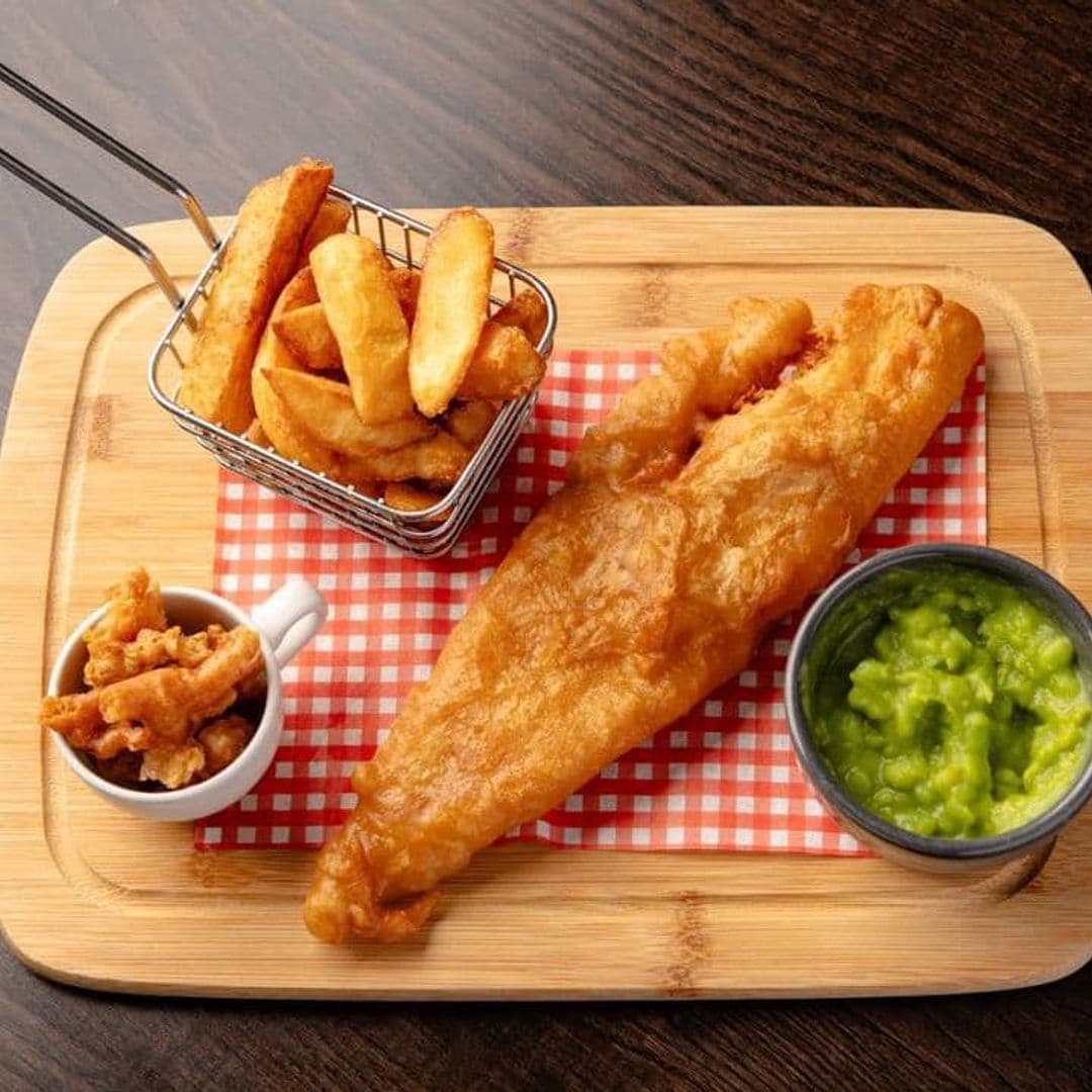 The Hare and Hounds Rothwell fish and chips traditional meal gastronomy restaurant Delicious fish and chips served at The Hare and Hounds – Rothwell. The dish features a large piece of golden-battered fish, crispy chips in a small basket, and a side of mushy peas. A small cup of crispy batter bits adds extra flavor. Perfect for a hearty meal.