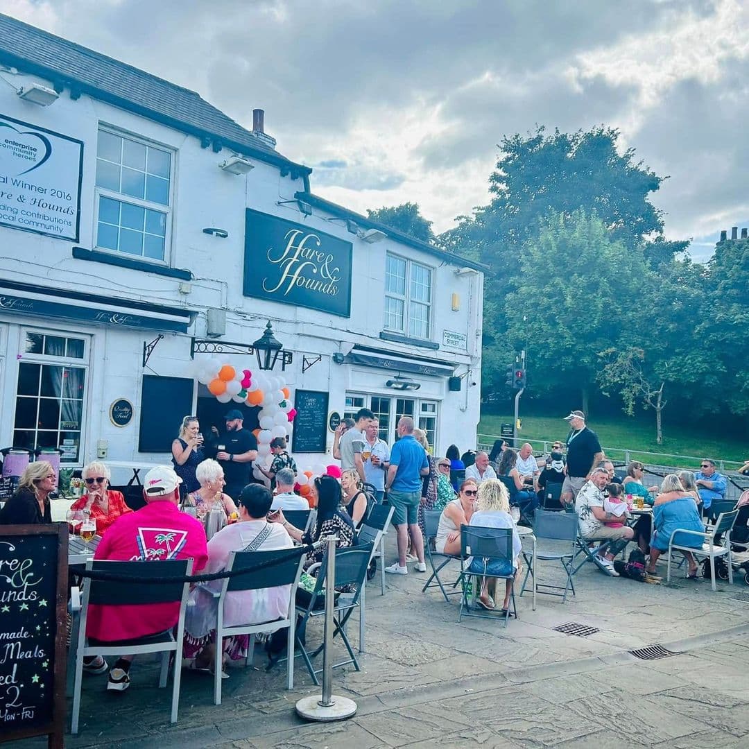 The Hare and Hounds Rothwell outdoor dining event summer festival crowd Outdoor dining scene at The Hare and Hounds – Rothwell, featuring a lively crowd enjoying meals and drinks. Colorful balloons are displayed, and people are seated at tables, creating a festive atmosphere. The pub's exterior is visible, showcasing its welcoming charm.