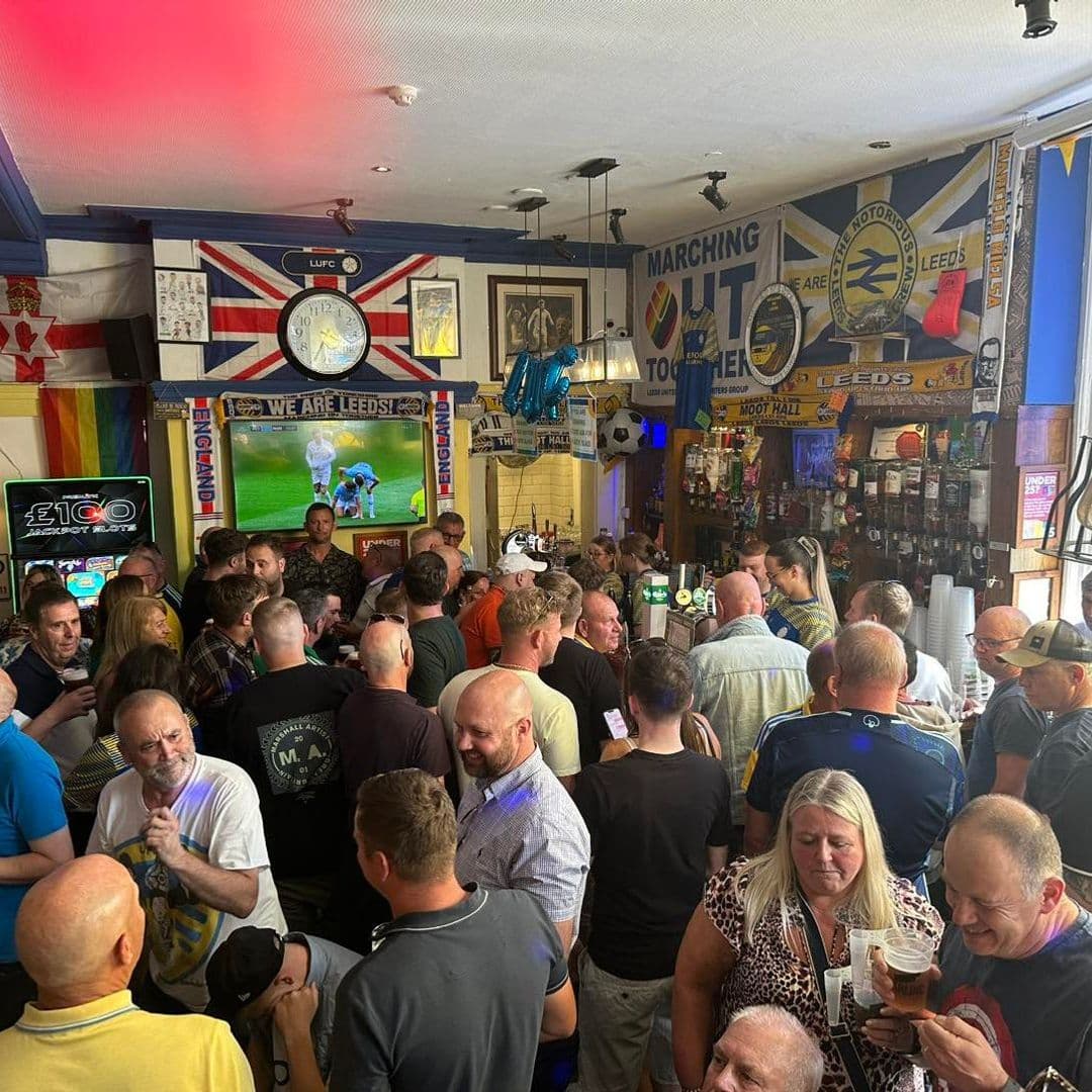 The Moot Hall Arms bustling pub crowd sports fans celebration Crowd of people enjoying drinks and socializing inside The Moot Hall Arms, decorated with sports memorabilia and flags. A large screen shows a sports event, creating a lively atmosphere.