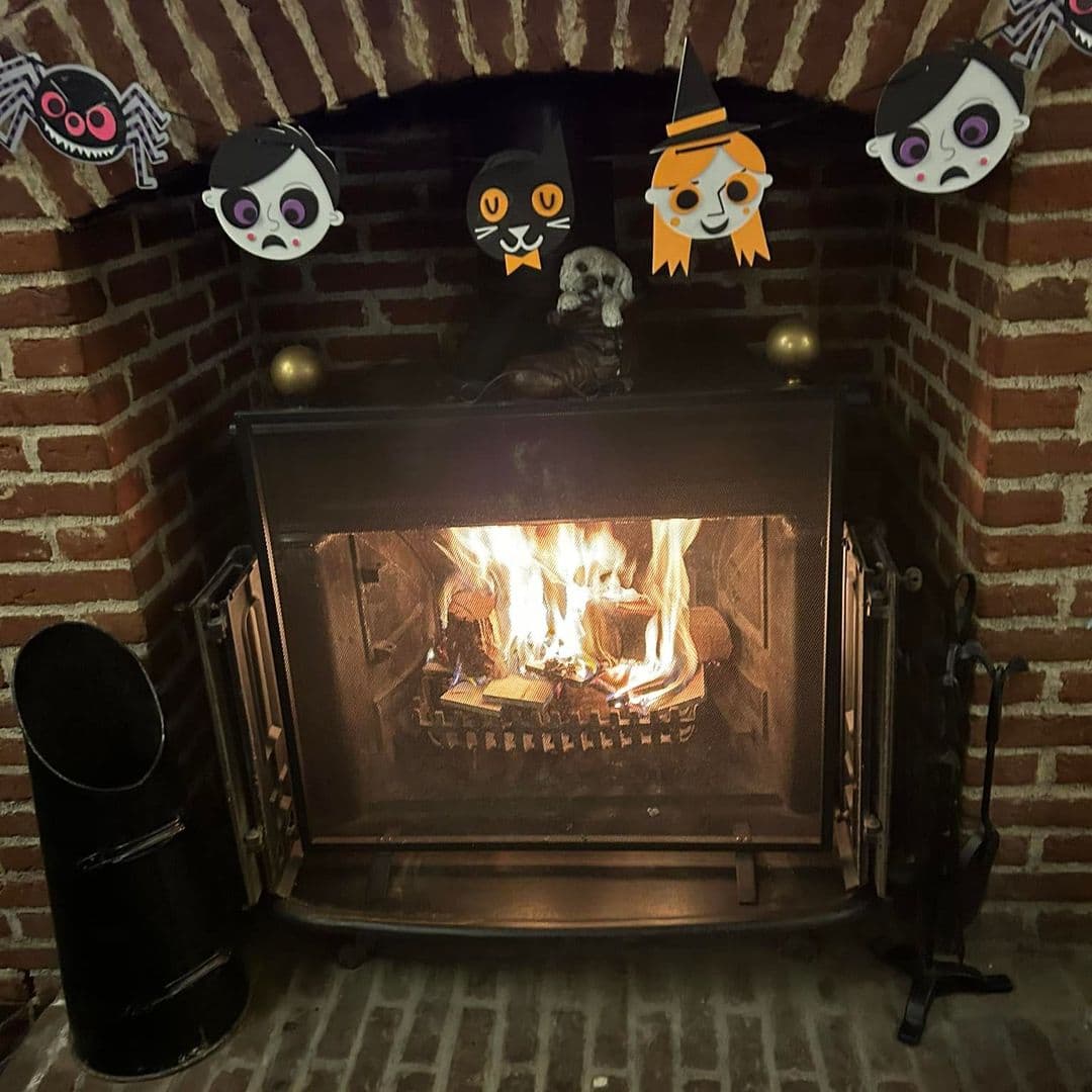 The Old Griffin Head cozy fireplace halloween decorations warmth A cozy fireplace with a warm fire burning inside, surrounded by a brick wall. Above the fireplace, there are playful Halloween-themed decorations, including a spider, a cat, and cartoon faces. The setting creates a welcoming and festive atmosphere at The Old Griffin Head.